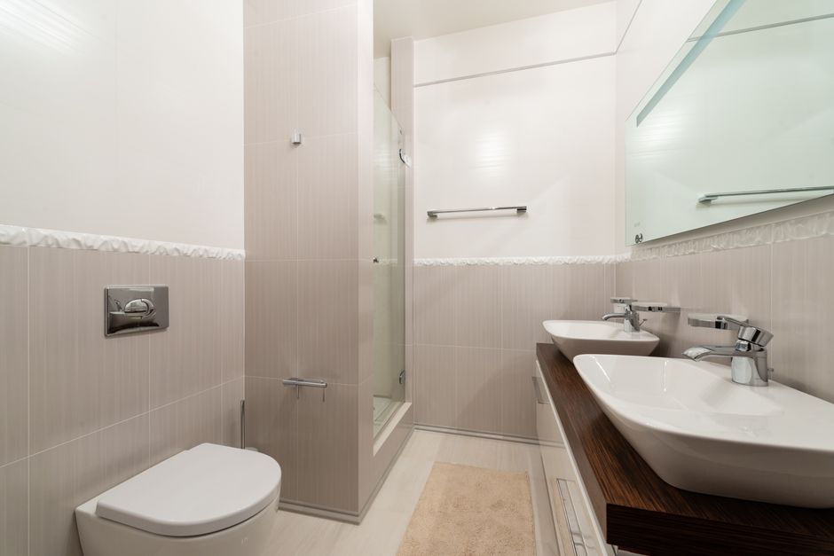 Bright and clean modern bathroom with shower, sinks, and toilet.